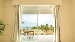 Une chambre dotée d’une porte-fenêtre coulissante donnant sur un balcon avec vue sur la plage et les palmiers.