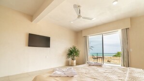 Une chambre d’hôtel avec un lit, un ventilateur de plafond, un téléviseur fixé au mur, une plante et une vue sur la plage.