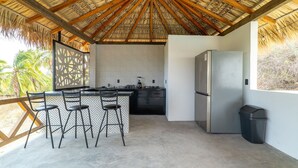 Une cuisine moderne dotée d’un toit de chaume, d’un réfrigérateur et d’un coin bar avec des tabourets.