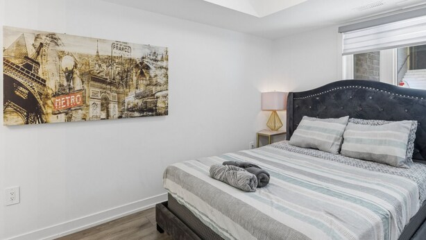 Quarto com cama, mesa de cabeceira, luminária e um pôster grande na parede.