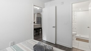 Quarto com cama, porta para um banheiro e uma cozinha compacta no cômodo vizinho.