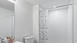 Casa de banho moderna com lavatório, sanita e zona de duche, tudo em branco.