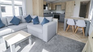 A modern, compact living space with a sofa, coffee table, and dining area. - Manor House Gold 2 Bedroom (Maryport)