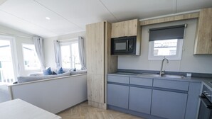 A modern kitchen with a built-in microwave, a sink, and a window seat with curtains. - Manor House Gold 2 Bedroom (Maryport)