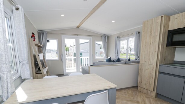 A modern kitchen with a wooden table and chairs, a built-in oven, and a view of the outside. - Manor House Gold 2 Bedroom (Maryport)