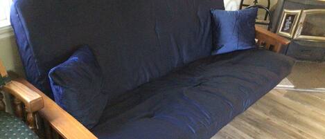 Un divano blu scuro con braccioli e cuscini in legno, appoggiato su un pavimento in legno.