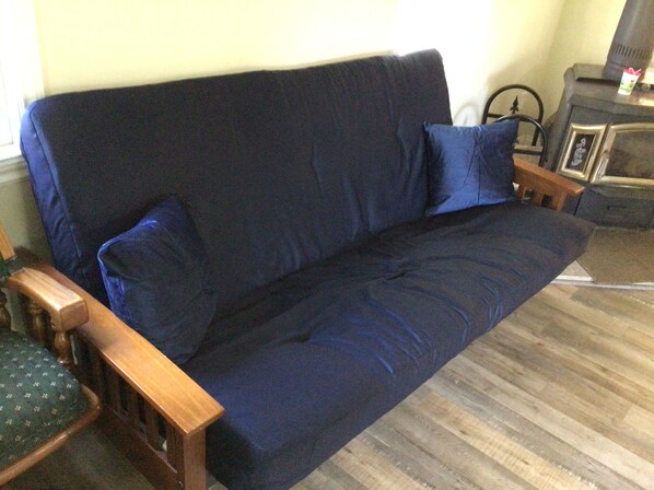 En mörkblÄ soffa med trÀarmstöd och kuddar, placerad mot en vÀgg med ett trÀgolv.