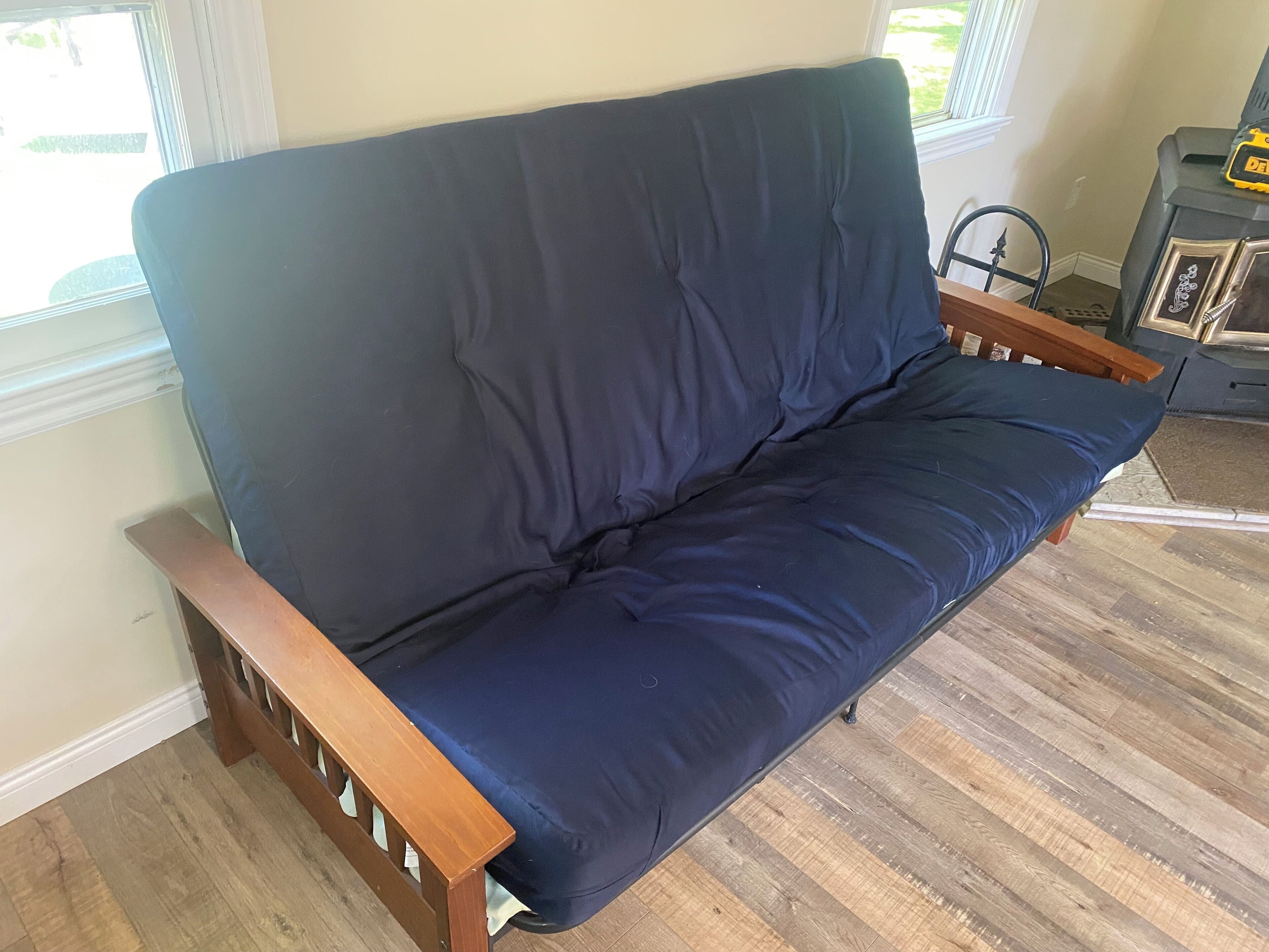 Un sofá azul oscuro con apoyabrazos de madera en una habitación con suelo de madera y un ventanal.