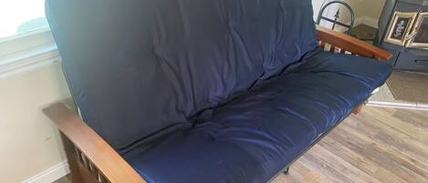 Un sofá azul oscuro con apoyabrazos de madera en una habitación con suelo de madera y un ventanal.