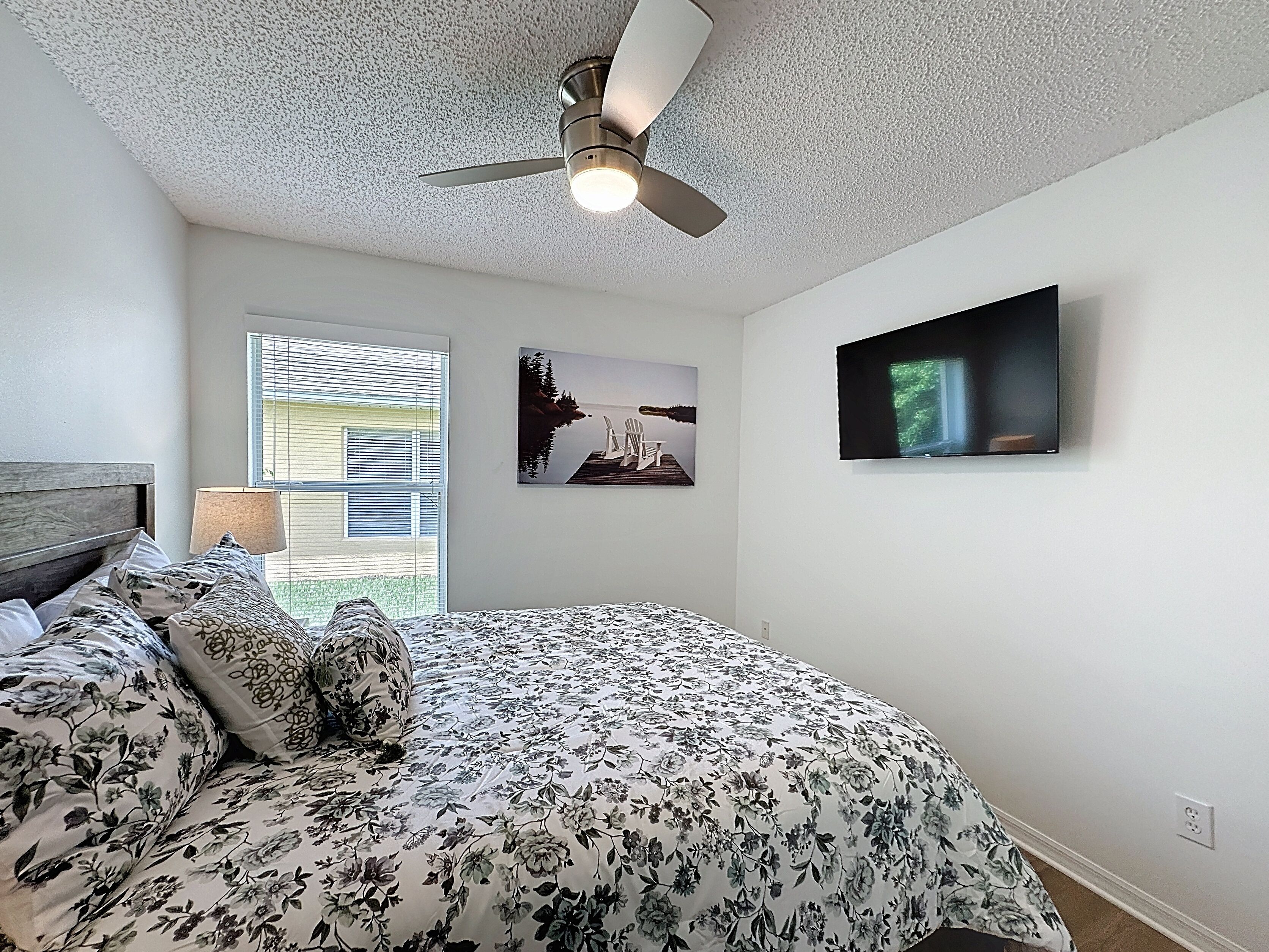 A bedroom with a bed, a ceiling fan, a TV, and two wall-mounted pictures.