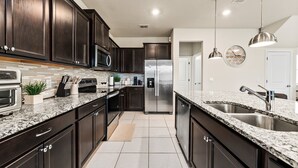 Una cocina moderna con armarios de madera oscura, electrodomésticos de acero inoxidable, encimeras de granito e iluminación colgante.