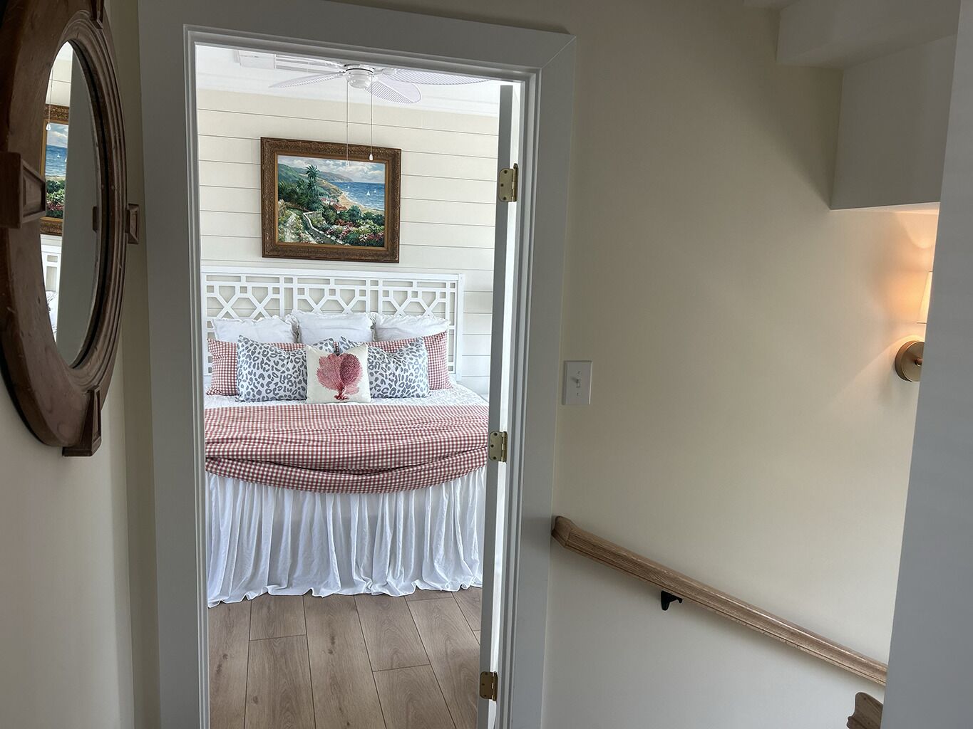 A doorway leading to a bedroom with a bed, a painting, and a ceiling fan.