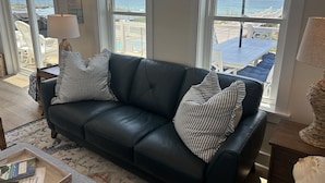A black leather sofa with striped pillows, a wooden coffee table, and a view of the beach through large windows.