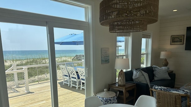 A spacious living area with a large sliding glass door leading to a wooden deck overlooking the beach.