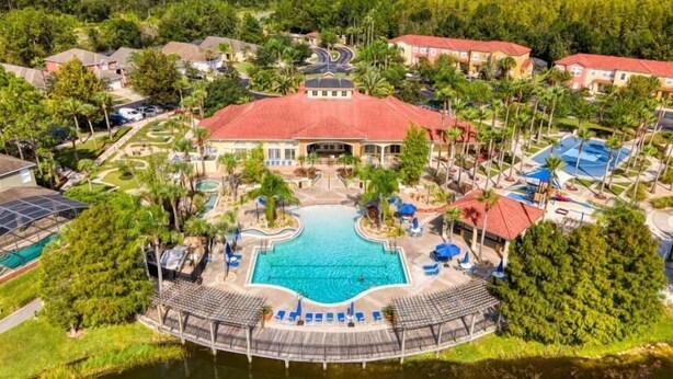 An aerial view of a resort with a central swimming pool, surrounded by palm trees and a lake. - Modern 3BR 2.5BTH Terra Verde Home with Private Hot Tub! (Kissimmee)