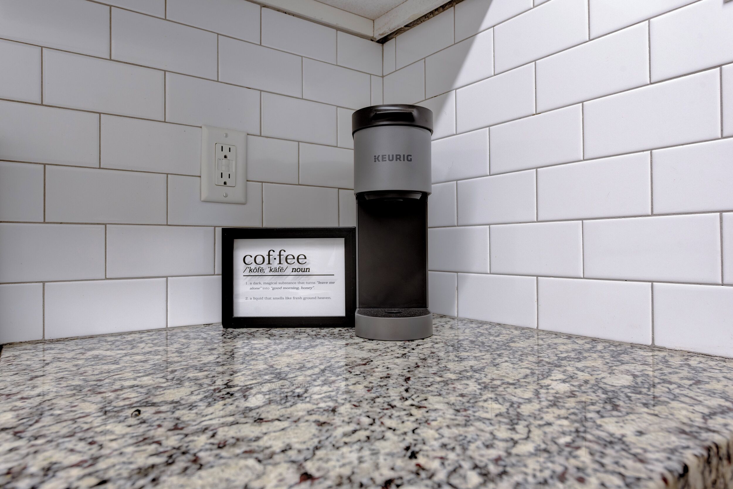 A kitchen counter with a framed coffee sign and a black water bottle.