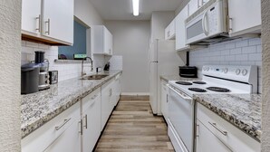 Cozinha pequena com armários brancos, bancada de granito, fogão branco e micro-ondas.