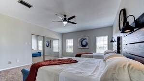 Quarto com duas camas, um ventilador de teto, um espelho grande e obras de arte nas paredes.