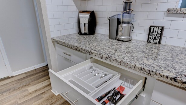 Cozinha com bancada de granito, cafeteira, dispensador de água e organizador de gaveta com utensílios.