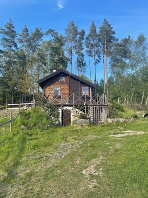 A wooden cabin with a metal bridge, surrounded by tall trees and a grassy area. - Cottage in historic Mariefred (Södermanlands län)