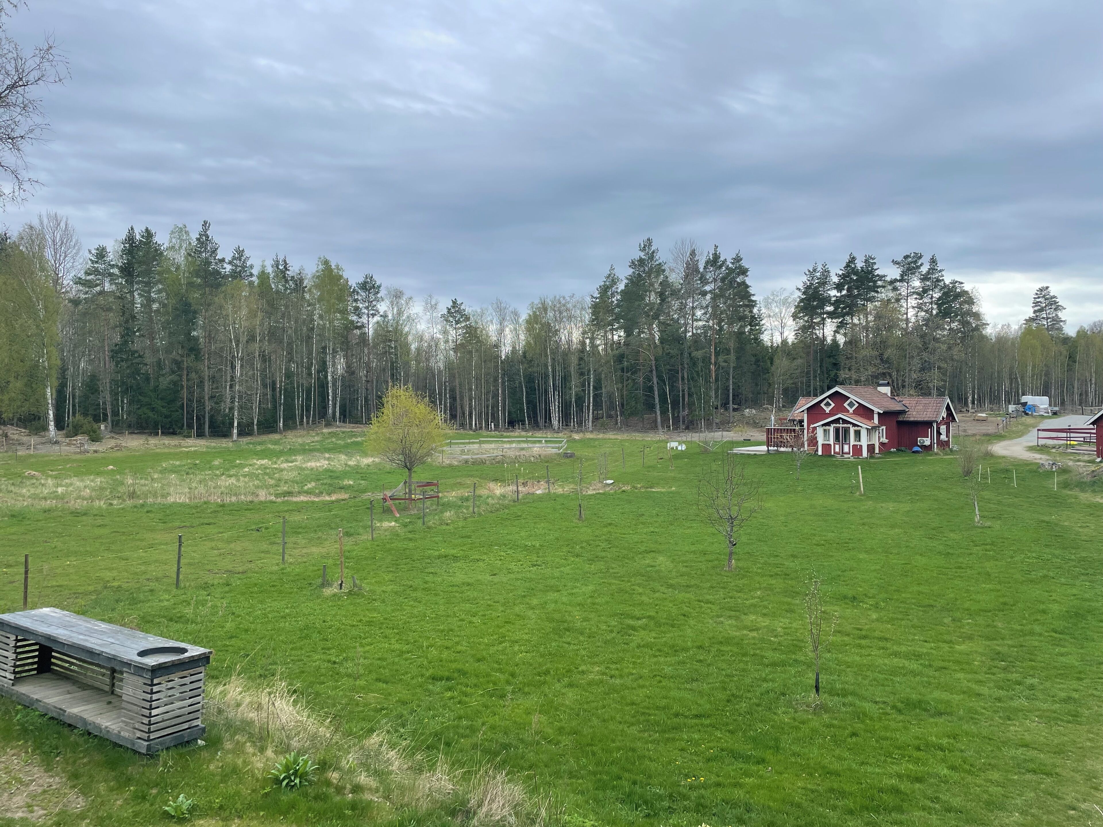 Un paysage rural avec une maison rouge, un champ clôturé et un petit abri.