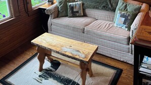 Ein gemütliches Zimmer mit Holzwänden, einem gestreiften Sofa, einem Holztisch und einem Fenster mit Vorhängen.
