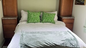 Ein Schlafzimmer mit einem Bett, grünen Kissen mit Muster, einer weißen Steudecke und Holzkopfseiten.