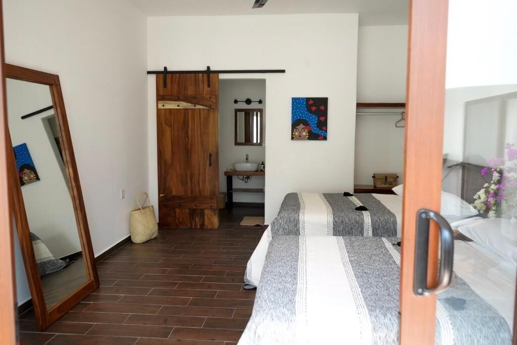 Een slaapkamer met twee bedden, een houten garderobe, een badkamer met een wastafel en een spiegel.