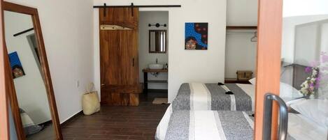 Un dormitorio con dos camas, un armario de madera, un baño con lavamanos y un espejo.