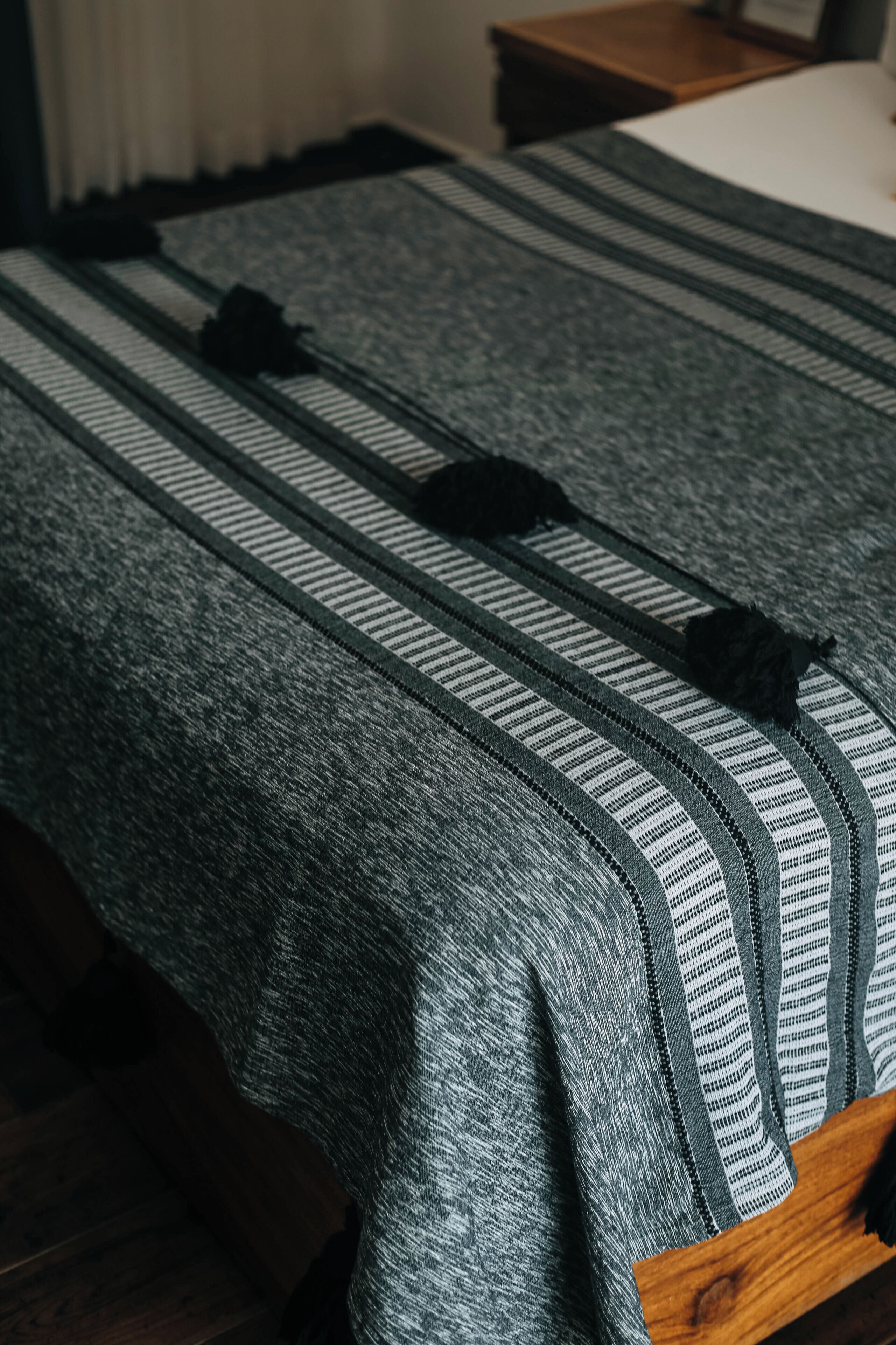 A bed with a striped blanket and black tassels, a wooden headboard, and a wooden nightstand with a lamp.
