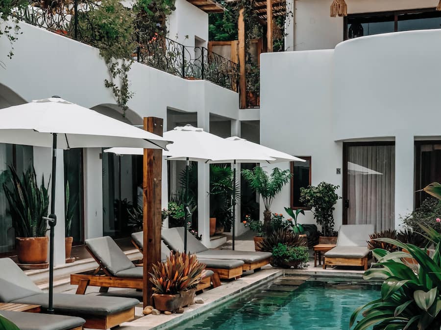 A pool area with lounge chairs and umbrellas, surrounded by potted plants and a white building.