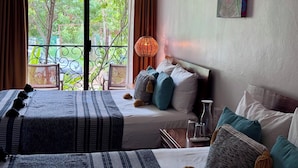 Quarto de hotel com uma grande janela, uma cama com roupa de cama listrada, uma mesa de cabeceira com copos e um painel decorativo na parede.