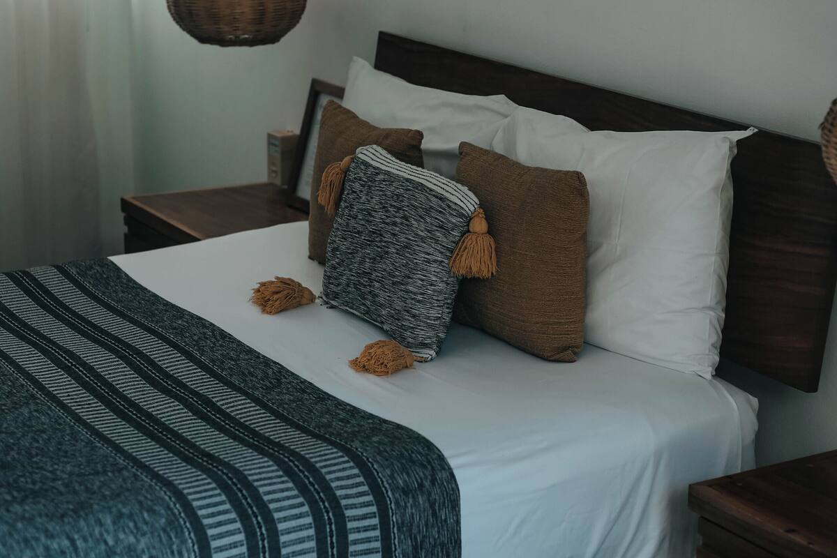 Una cama bien hecha con una colcha a rayas, una lámpara colgante y un cuadro en la pared.