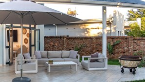 An outdoor patio area with a white sofa, a coffee table, and a large umbrella. - Stunning 3 Bedroom House Near Harare Airport -2297 (Harare)