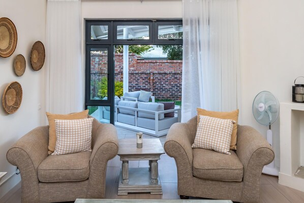 A living room with two armchairs, a coffee table, and a view of a patio with a sofa and a brick wall.