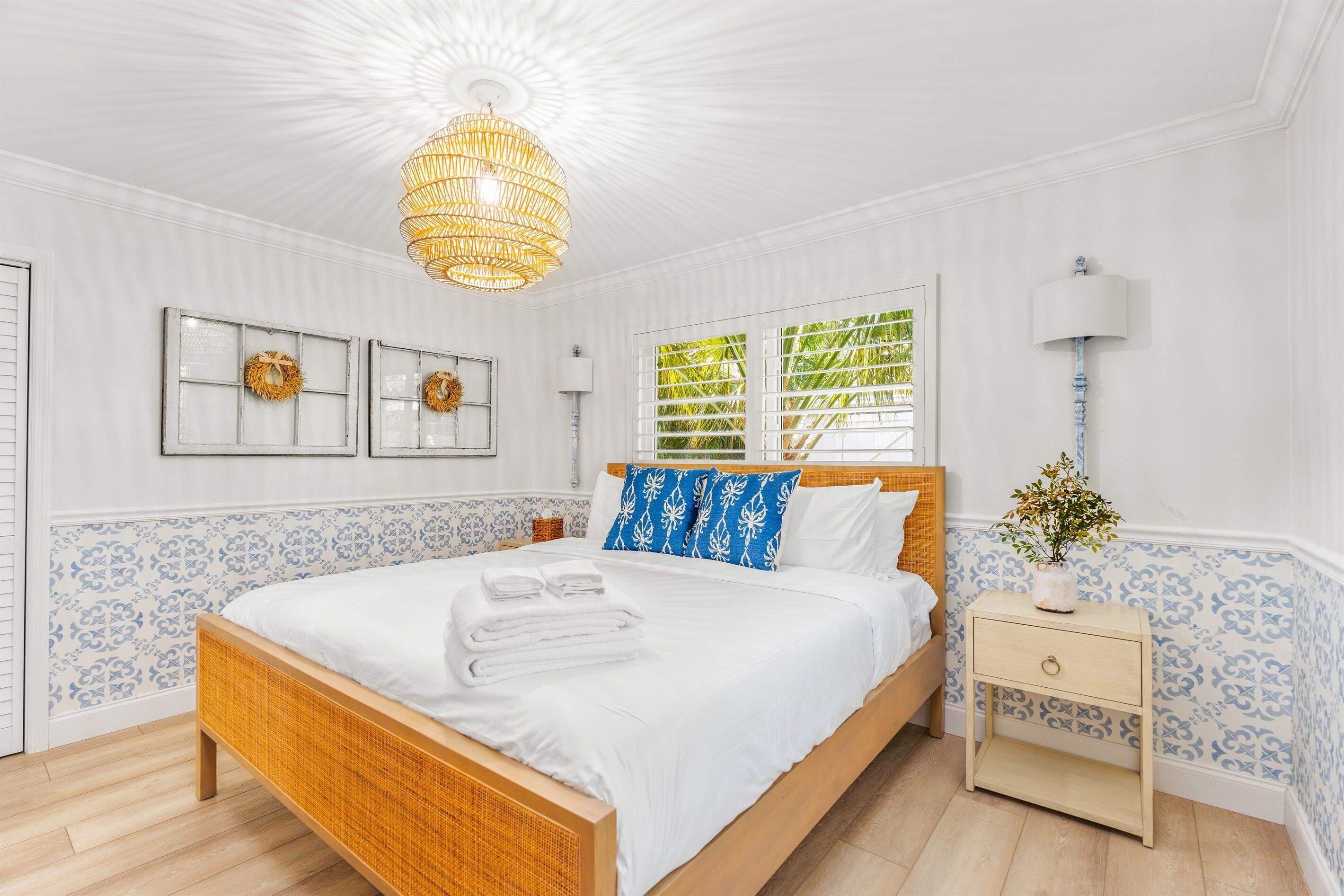 A neatly arranged bedroom with a large bed, a bedside table, a hanging light fixture, and a window with blinds.