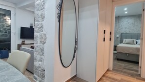 A modern interior with a stone accent wall, a large mirror, a dining area with a marble table, and a bedroom with a bed and nightstand. - Sea view Charming 1-bedroom apartment with AC, WiFi in enchanting Tivat (Tivat)