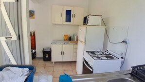 A compact kitchen with white cabinets, a gas stove, a microwave, and a refrigerator. - House, located on the Guadeloupe coast. 25min. from the volcano. (Vieux-Fort)