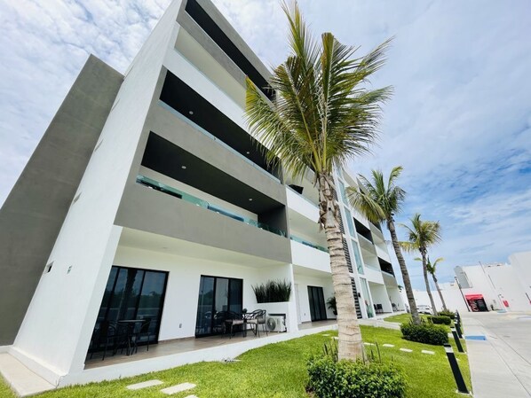 A modern multi-story hotel with balconies, outdoor seating, and palm trees.