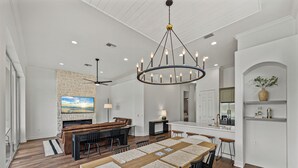 Amplia sala de estar con una mesa de comedor de madera, sillas negras, una chimenea de piedra y una gran pantalla de televisión.