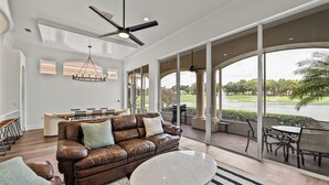 Un salón amplio con un sofá de cuero marrón, una mesa de centro redonda y un ventanal con vistas a un campo de golf.