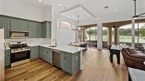 Una cocina amplia con una isla grande, un comedor con vista a un campo de golf y una zona de estar acogedora con vistas al exterior.