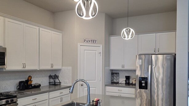 A modern kitchen with white cabinets, a stainless steel refrigerator, and pendant lighting. - Family-Friendly 5BR Home, Game Room + Large Backyard! with AC, WiFi in 77407 (Richmond)