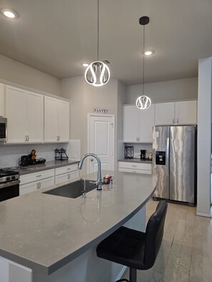A modern kitchen with white cabinets, a stainless steel refrigerator, and pendant lighting. - Family-Friendly 5BR Home, Game Room + Large Backyard! with AC, WiFi in 77407 (Richmond)