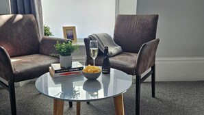 A modern living room with two leather armchairs, a glass coffee table, a small potted plant, a bowl of chips, a bottle of champagne, and a book titled "Westwind". - Spacious Penthouse | Central  Location | 3 Doubles (Plymouth)