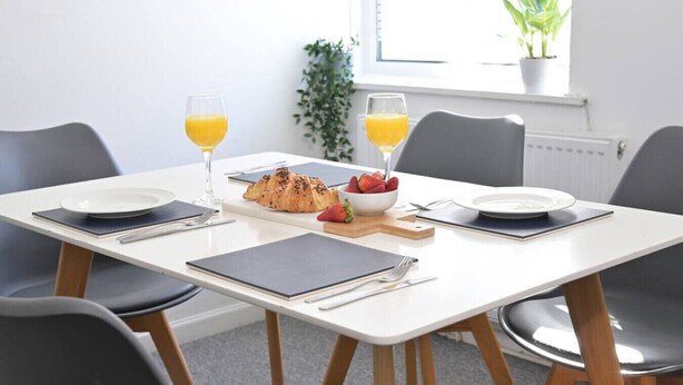 A dining table set with plates, cutlery, a croissant, strawberries, and glasses of orange juice. - Spacious Penthouse | Central  Location | 3 Doubles (Plymouth)