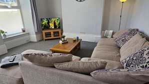 A living room with a beige sofa, a wooden coffee table, and a television on a stand. - Spacious Penthouse | Central  Location | 3 Doubles (Plymouth)