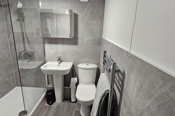 A modern bathroom with a glass shower enclosure, a pedestal sink, a toilet, and a towel rack.
