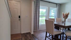 A spacious room with a wooden floor, a dining table with chairs, a window with curtains, and a door. - Spacious 4-bedroom Mas in Delightful Palm Coast with AC, WiFi (Palm Coast)