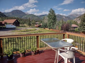 Un terrazzo in legno con tavolo e sedie in vetro, piante in vaso e vista sulle montagne e sulle case.